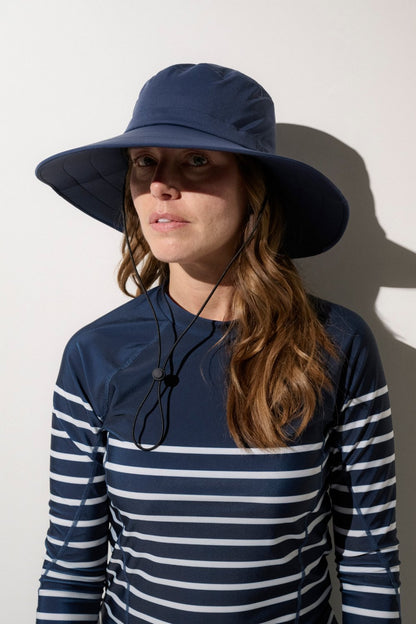 Femme portant un chapeau de bain anti-UV Ker Sun, léger et pratique, avec un maillot rayé UPF 50+ pour une protection solaire.